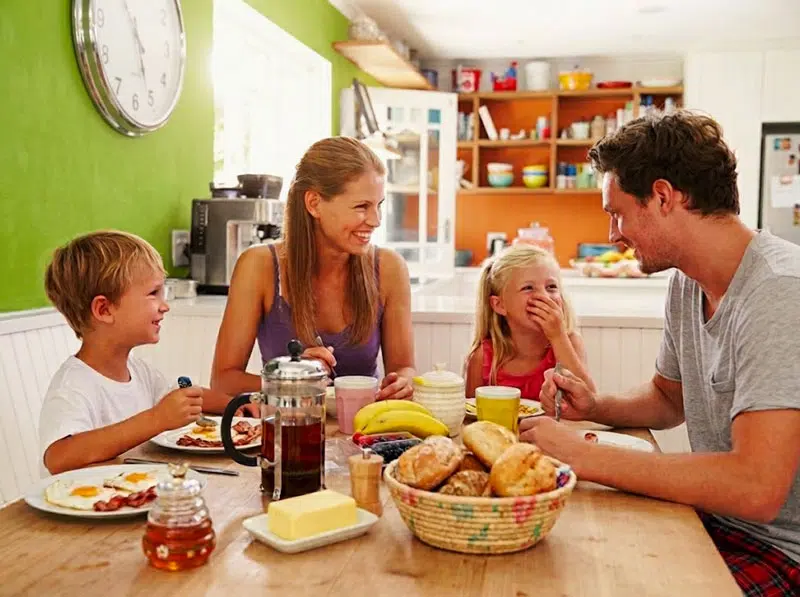 Familie beim Frühstück in der Küche: Vater, Mutter, Sohn und Tochter sitzen lachend am Holztisch mit Spiegeleiern, Brötchen, Tee und Obst. © 123rf.com #41461610, bearbeitet.